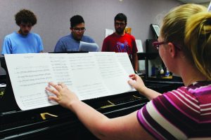 Aca-Practice: Pianist Kirsten Fuchs organizes her music sheets while her fellow vocalists practrice the club's latest song "Wrecking Ball" by Miley Cyrus. Photo by Genesis Rodrigues - Staff Photographer